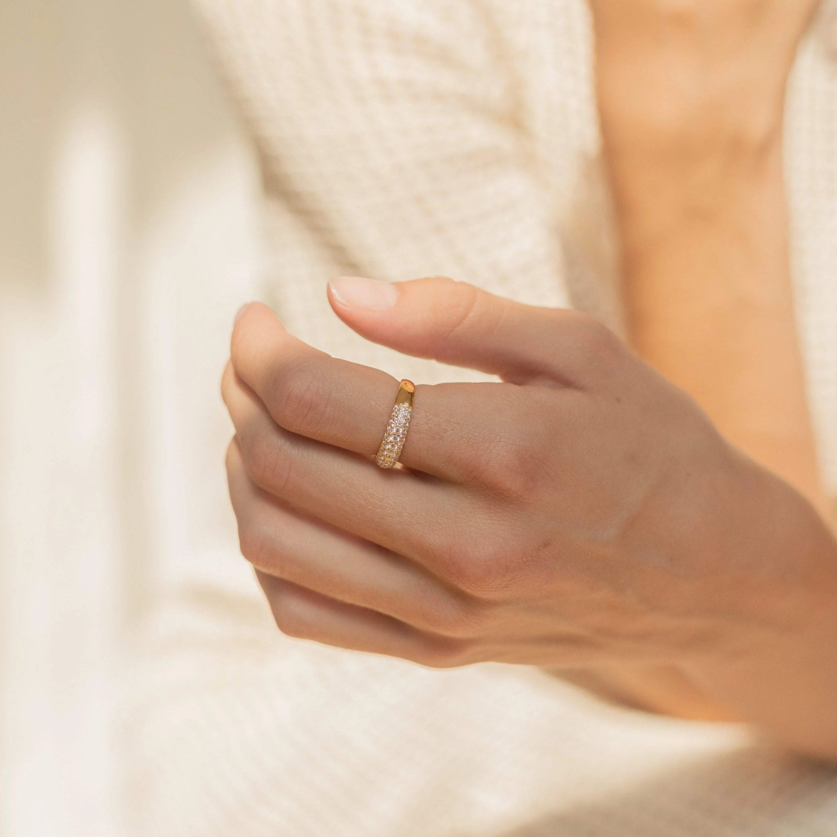 Hand wearing a gold ring with a soft focus background
